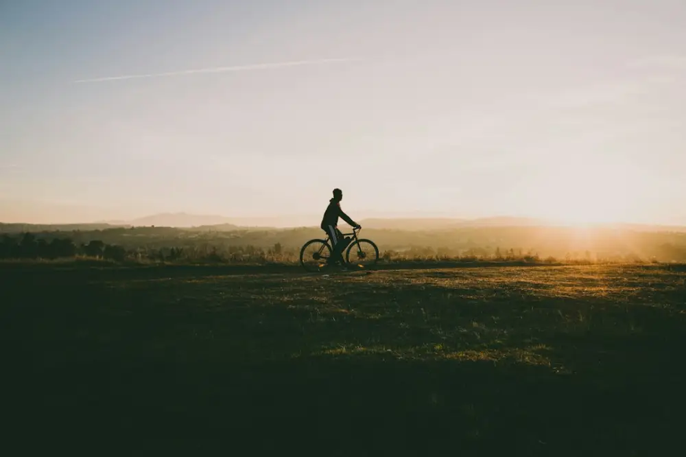 Person riding bicycle near grass in sunset, illustrating everyday joy and confidence on a bicycle